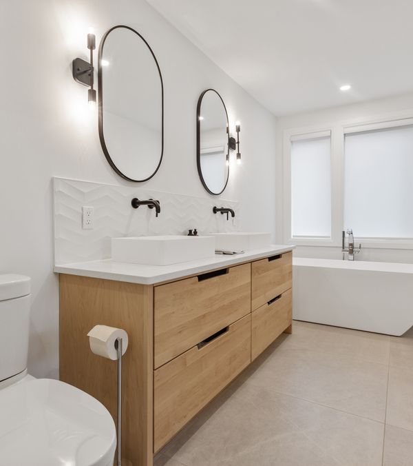 Badezimmer mit Toilette, Badewanne und hölzerner Kommode unter den beiden Waschbecken.